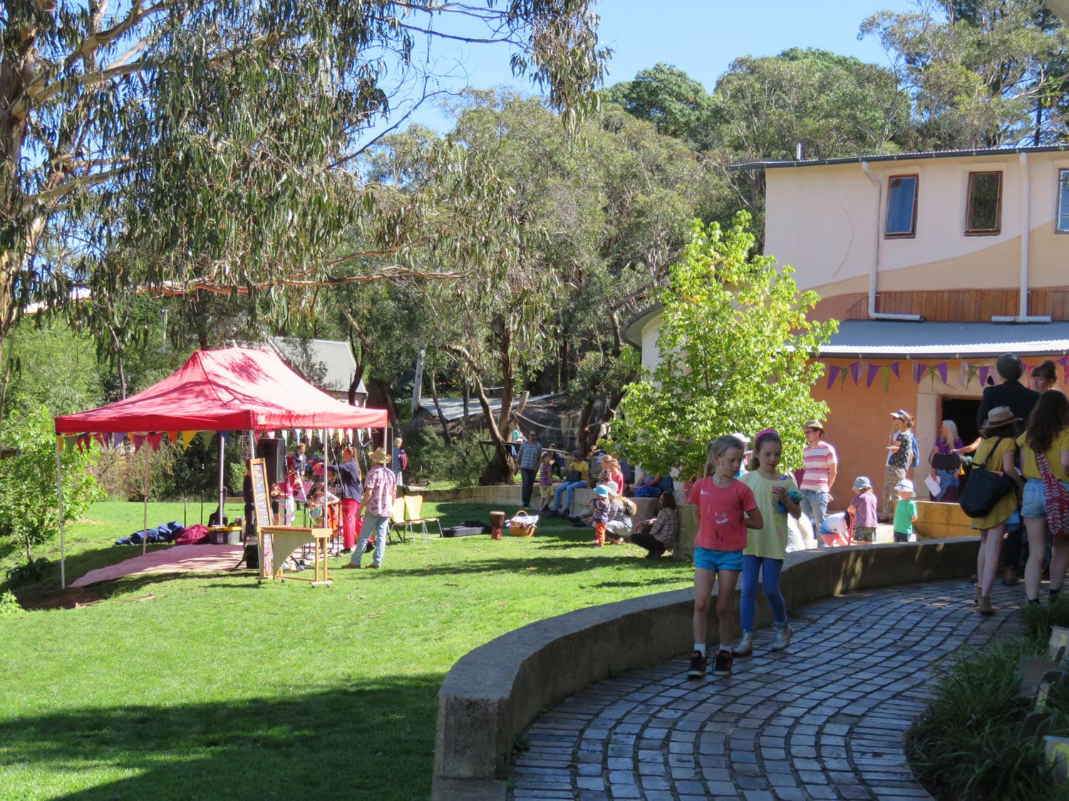 Families and children celebrate a vibrant Kindlehill fair, weaving community connection and creative joy through the bushland setting.