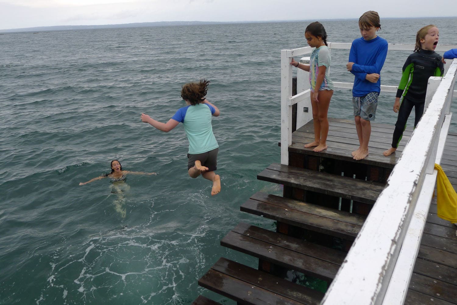 Kindlehill students leap from a wooden jetty into the bay, fostering resilience and connection through shared outdoor adventure.