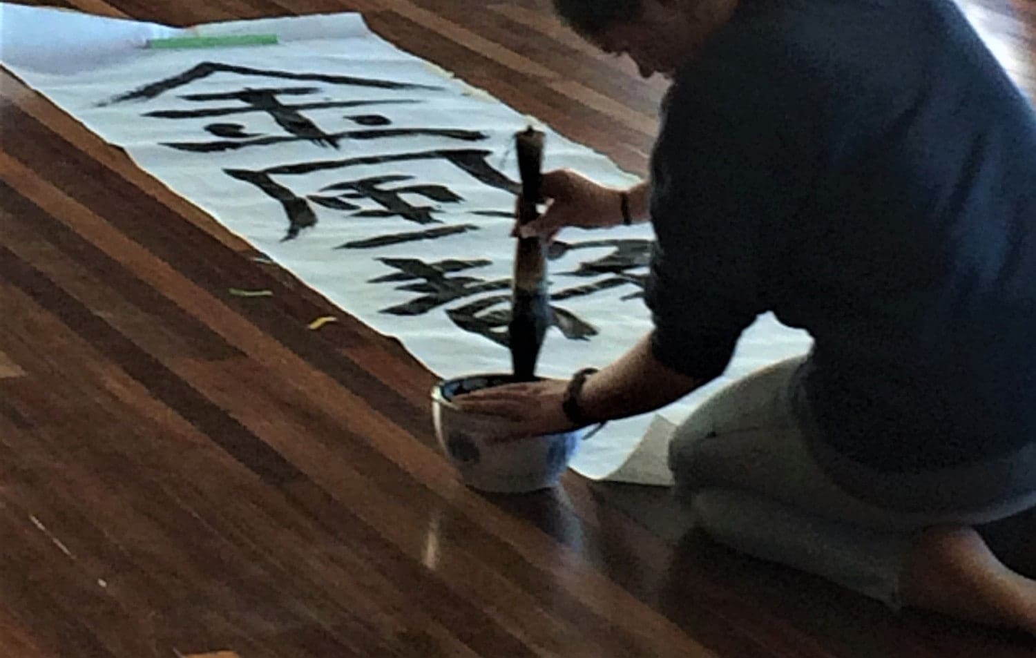 A student paints Japanese calligraphy on a floor scroll, honouring global friendship through artistic expression and peace ceremony.