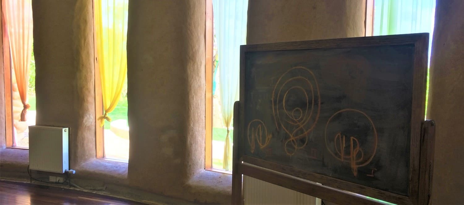A chalkboard displays rhythmic eurythmy forms within sunlit earthen walls, fostering concentration, inner quiet, and communal harmony.