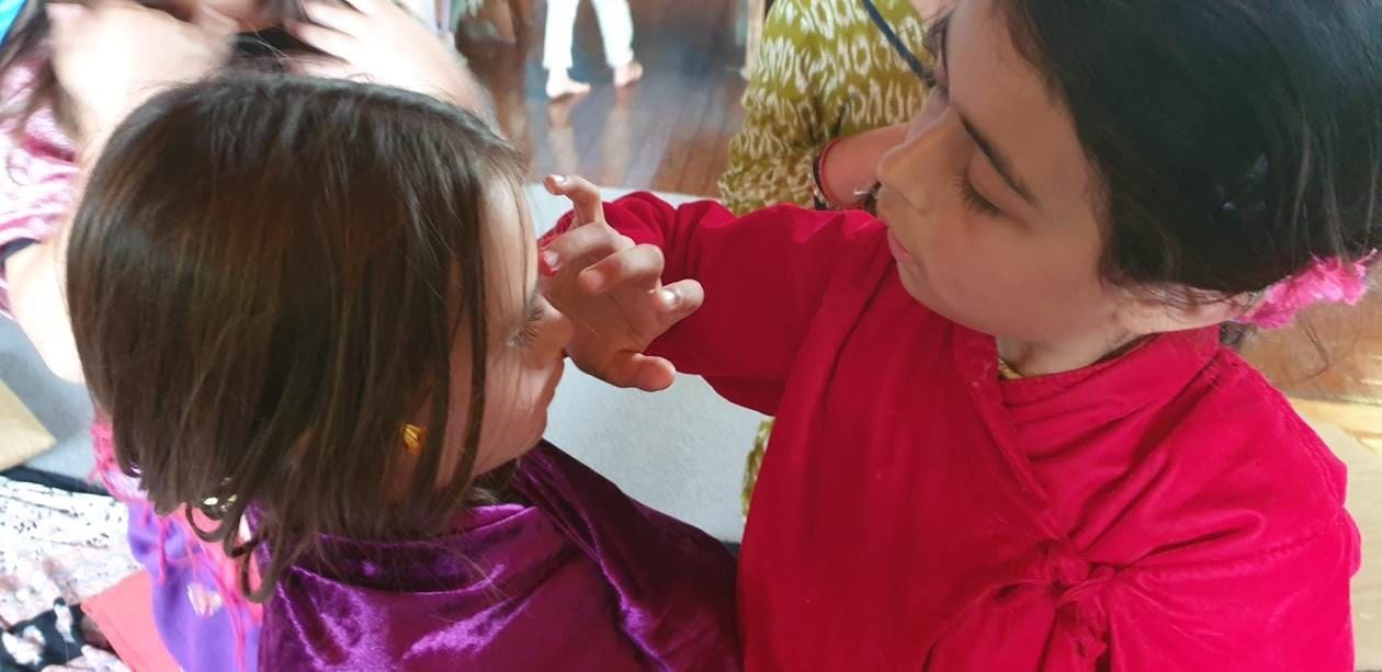 A child applies a sacred mark to their classmates forehead, honouring Ancient Indian traditions and community connection.