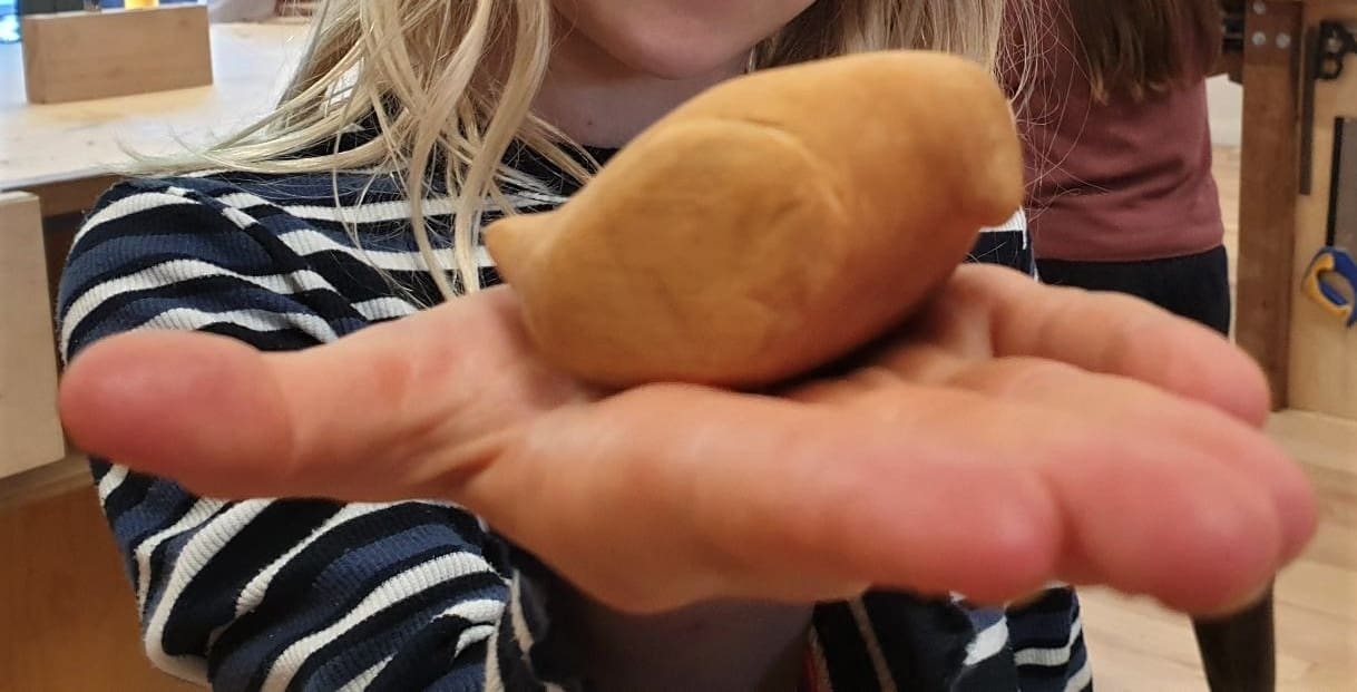 A students palm cradles a hand-carved wooden bird, demonstrating the creative connection between head, heart, and hands.