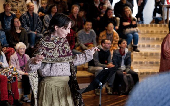 A conductor leads the Kindlehill village in song, uniting families through a shared rhythm of music and heartfelt connection.