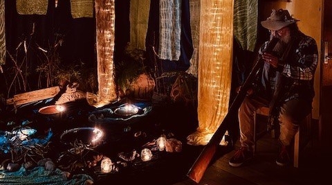 An Elder plays didgeridoo amidst glowing silks, honouring First Peoples stories and sacred connection to Country.