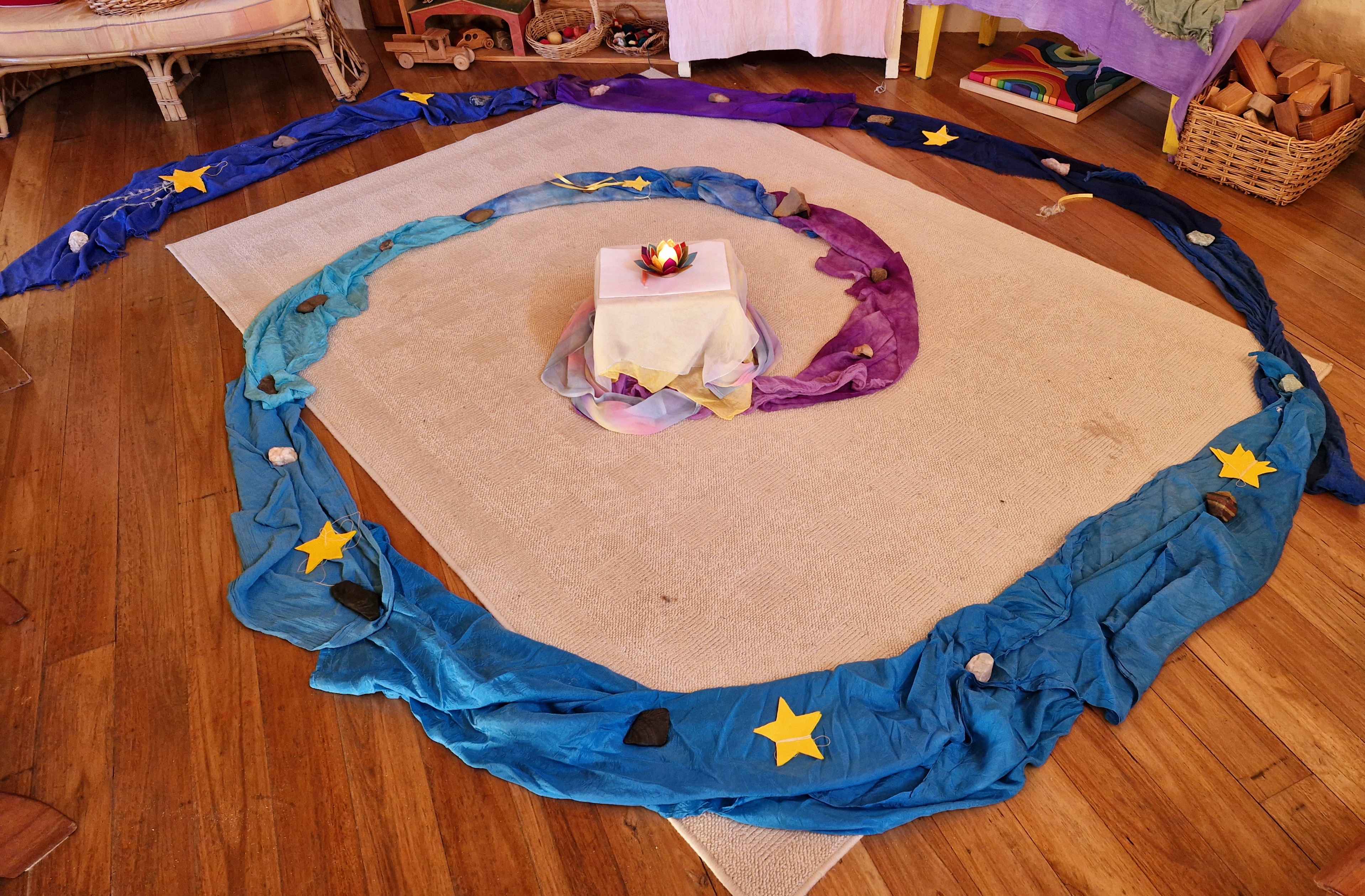A silk spiral adorned with stars leads to a central candle, guiding playgroup children toward their inner light.