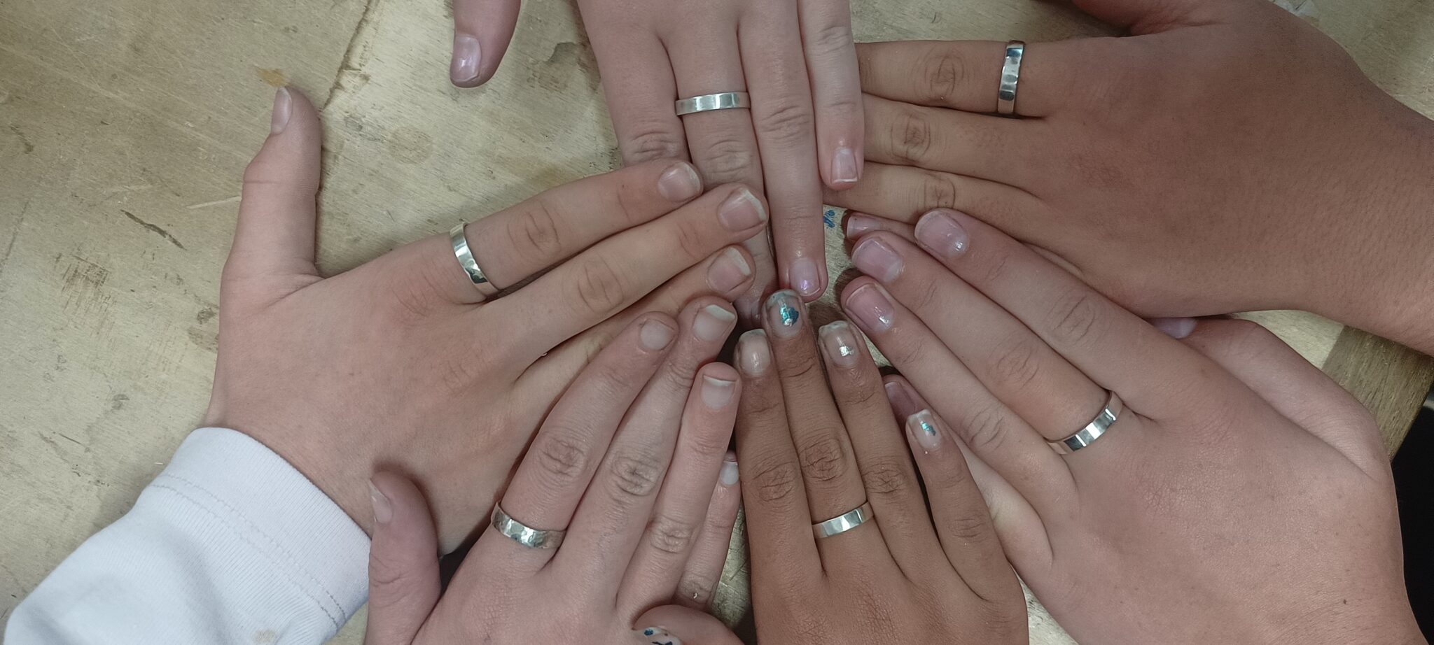 Student hands wearing handmade silver rings unite in a circle, symbolising the fusion of creative craftsmanship and community connection.