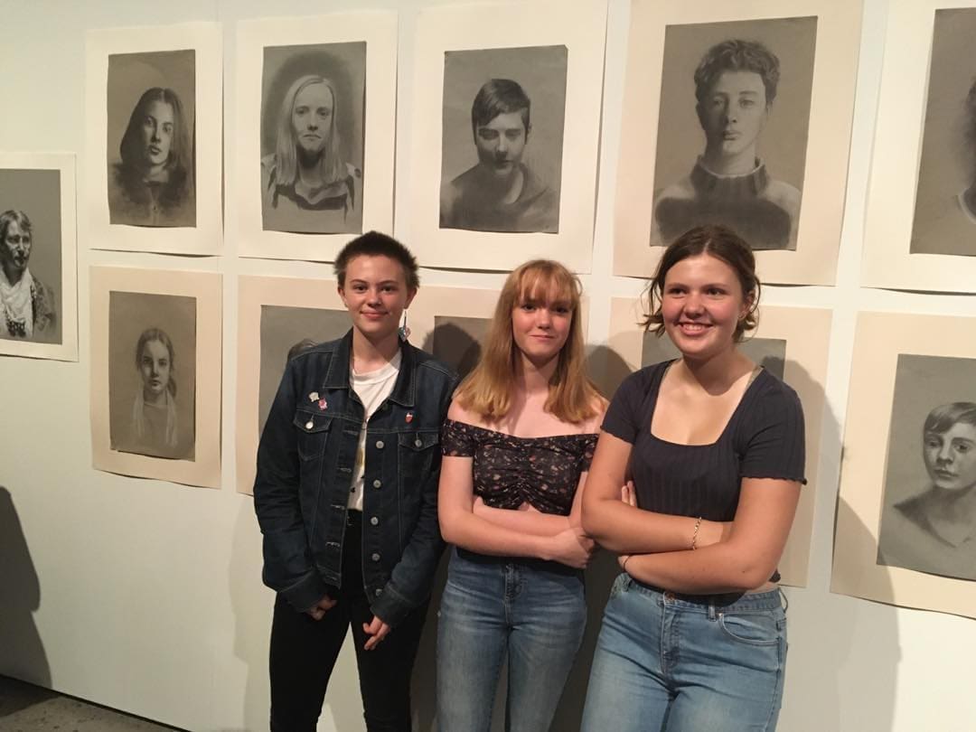 Kindlehill students stand before their hand-drawn portraits, celebrating the growth of whole humans through head, heart, and hands.
