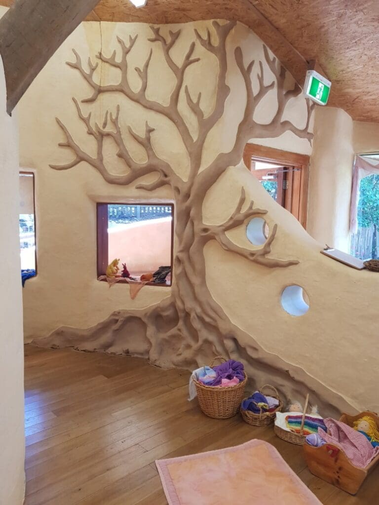 Hand-sculpted tree branches weave through warm earthen walls, grounding childrens creative play in the beauty of nature.