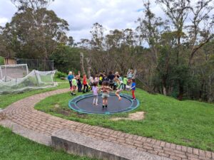Children jump together outdoors, fostering community spirit and a deep connection to the ancient Blue Mountains landscape.