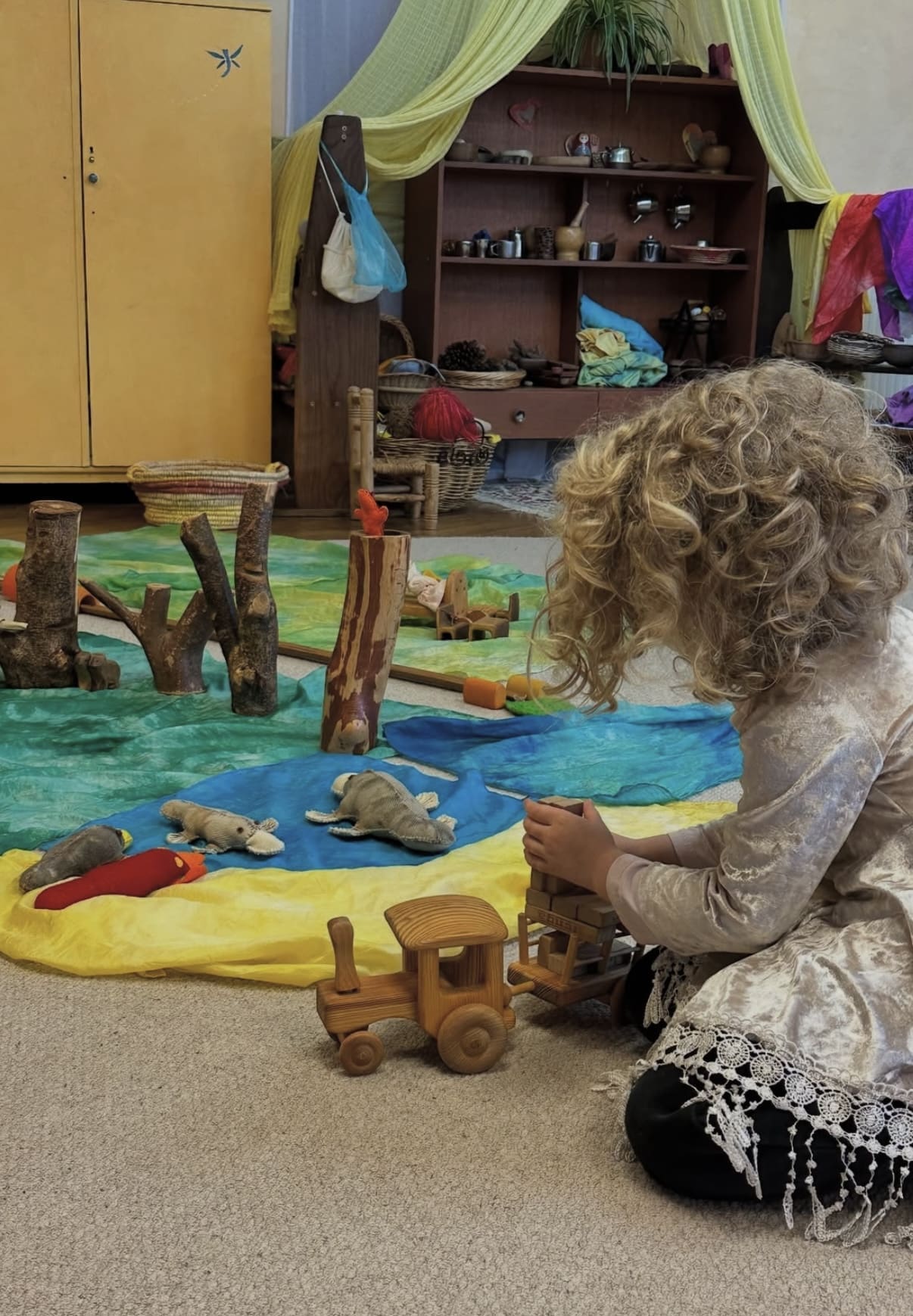 Child nurtures wonder through imaginative play with natural toys and colourful silks in a Steiner classroom environment.