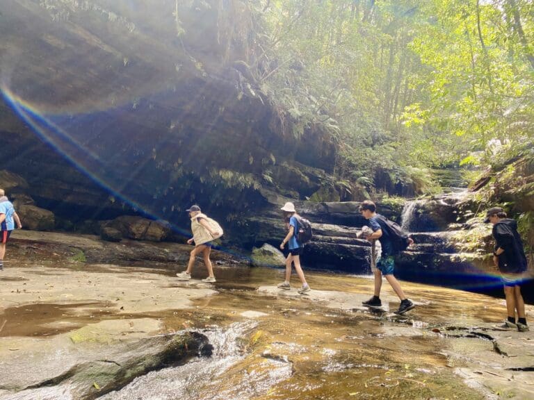 Students traverse a sunlit creek bed, honouring the land and deepening their connection to the Blue Mountains wilderness.