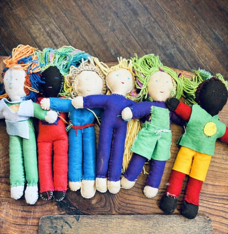 Hand-stitched dolls of diverse colours link together, celebrating a warm community where every child truly belongs.