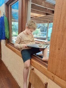 A barefoot Kindlehill student reads in a timber window nook, awakening imagination through wonder and the rhythm of storytelling.