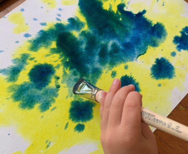 A childs hand paints with vibrant watercolours, expressing imagination and connection to nature through heart-centred artistic flow.