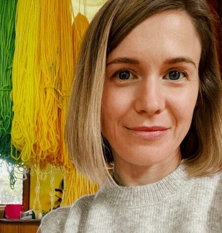 A Kindlehill member radiates warmth beside vibrant wool, celebrating artistic expression and the connection between heart and hands.