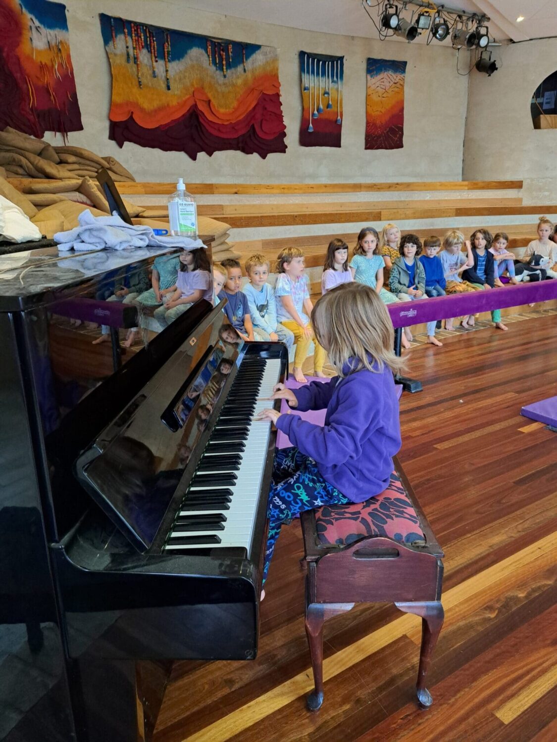 Students listen intently as a classmate plays piano, honouring artistic expression and the shared spirit of community.