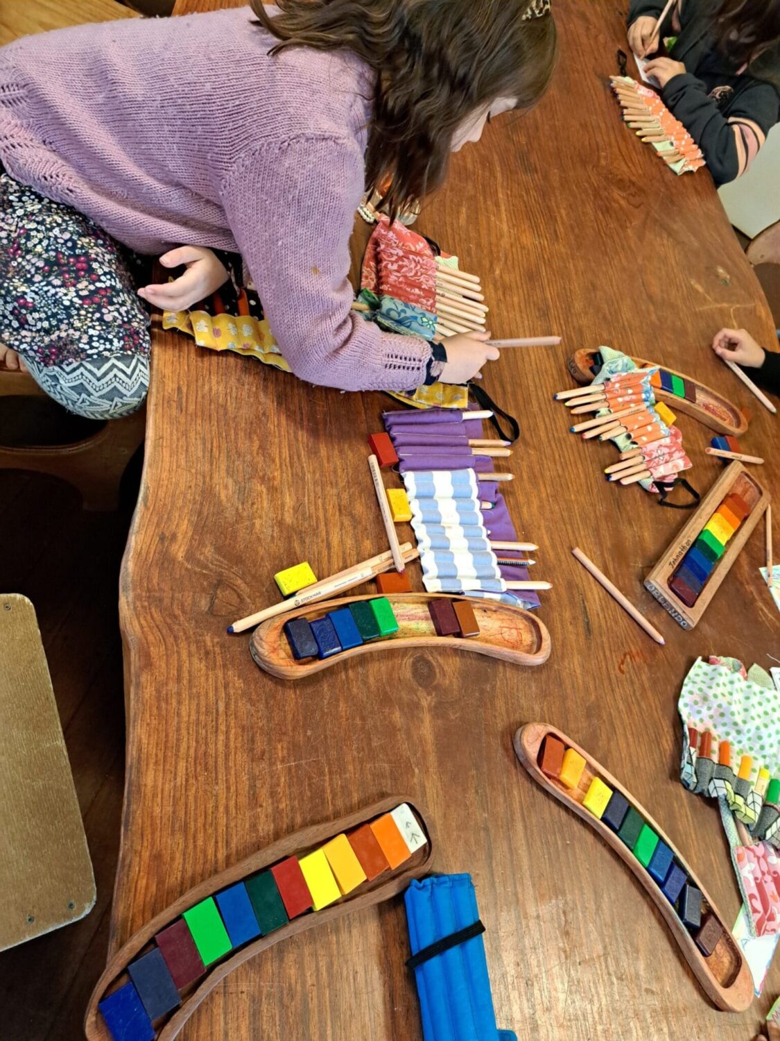 Children cultivate imagination and connection through artistic expression, using colourful pencils and block crayons at communal timber tables.